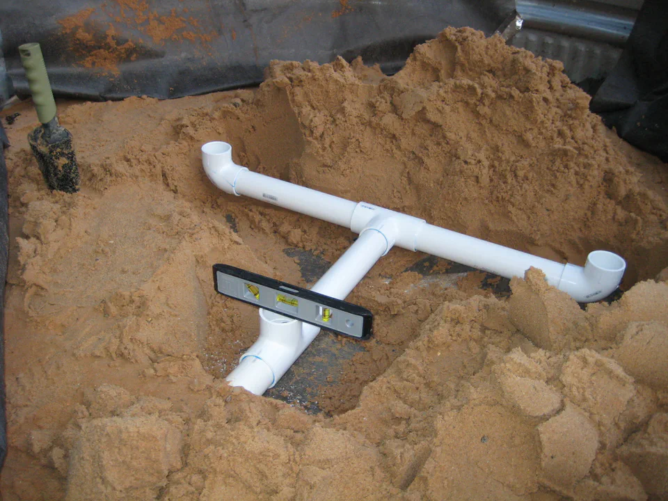 On the second bed, leveling the manifold dead flat in the sand so the reservoir fills evenly end to end.