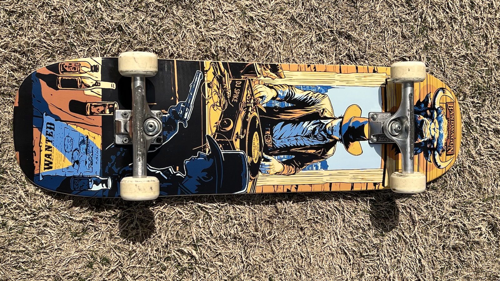 A skateboard deck with a graphic of a western cowboy DJ spinning a record on a turntable; my name is printed tiny on the record.