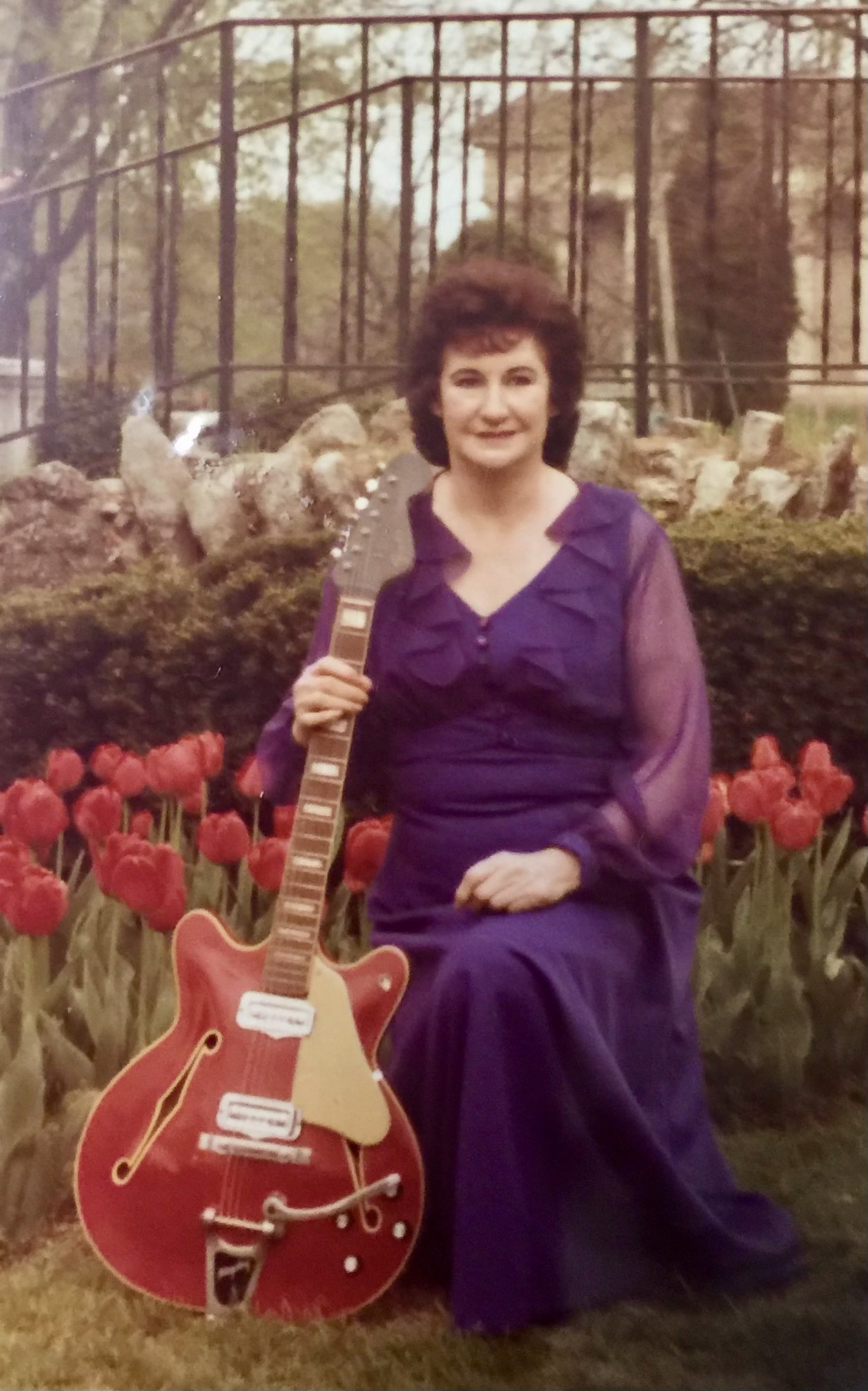 A 1970s portrait of my grandmother holding the same Fender, in a purple dress.